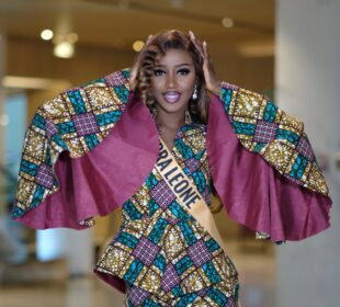 Sierra Leone contestant in an African wax-print outfit with wide cape sleeves and a Sierra Leone sash