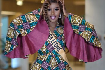 Sierra Leone contestant in an African wax-print outfit with wide cape sleeves and a Sierra Leone sash