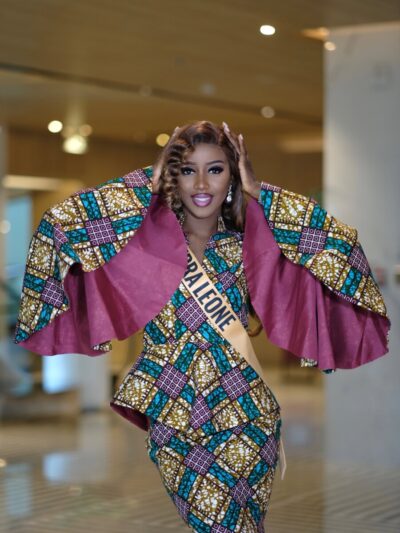 Sierra Leone contestant in an African wax-print outfit with wide cape sleeves and a Sierra Leone sash