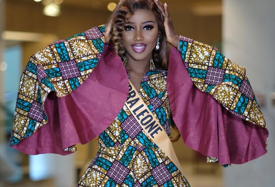 Sierra Leone contestant in an African wax-print outfit with wide cape sleeves and a Sierra Leone sash